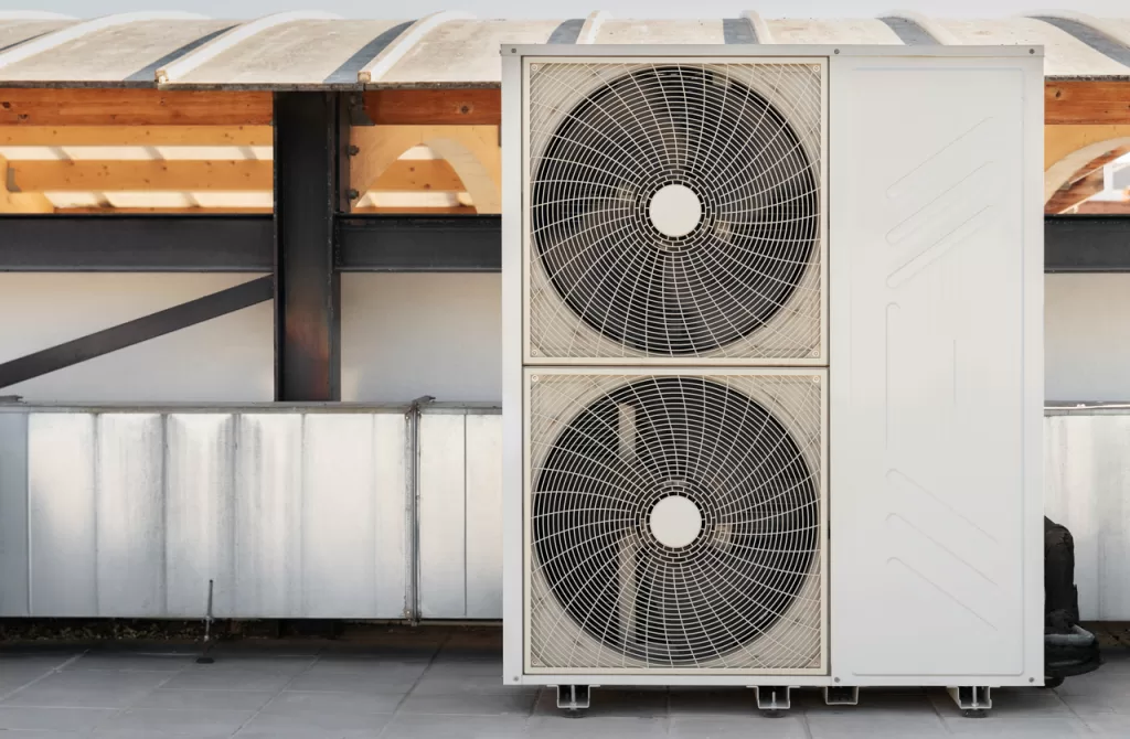 A commercial air conditioning unit with two large fans is positioned outdoors, supported by a steel structure with a partially covered roof, emphasizing industrial cooling solutions.