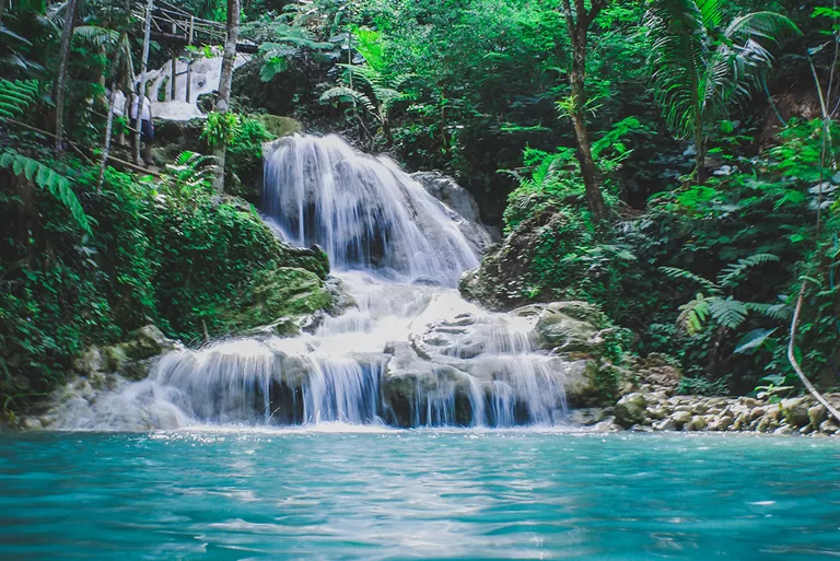 A beautiful cascading waterfall flowing into a turquoise pool, surrounded by dense tropical greenery, creating a serene and refreshing atmosphere.