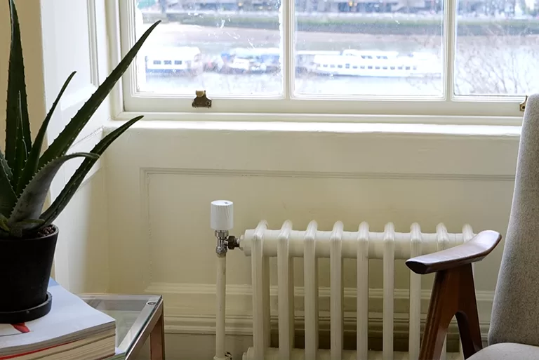 Smart Radiator in a cozy indoor scene featuring a classic radiator fitted with a modern VEXO S-TRV smart thermostat near a window, optimizing heating efficiency.
